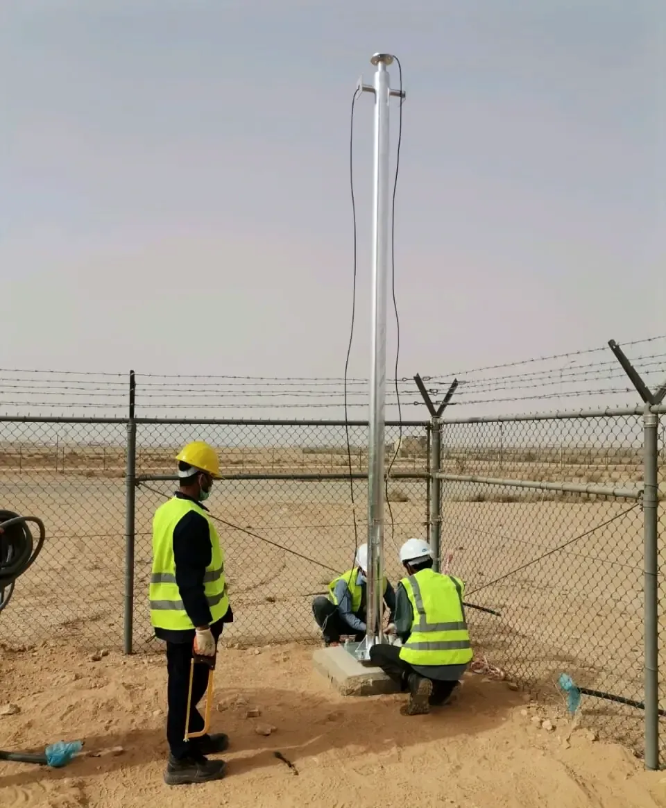 Site engineers in hard hats raising a mast inside a fenced compound